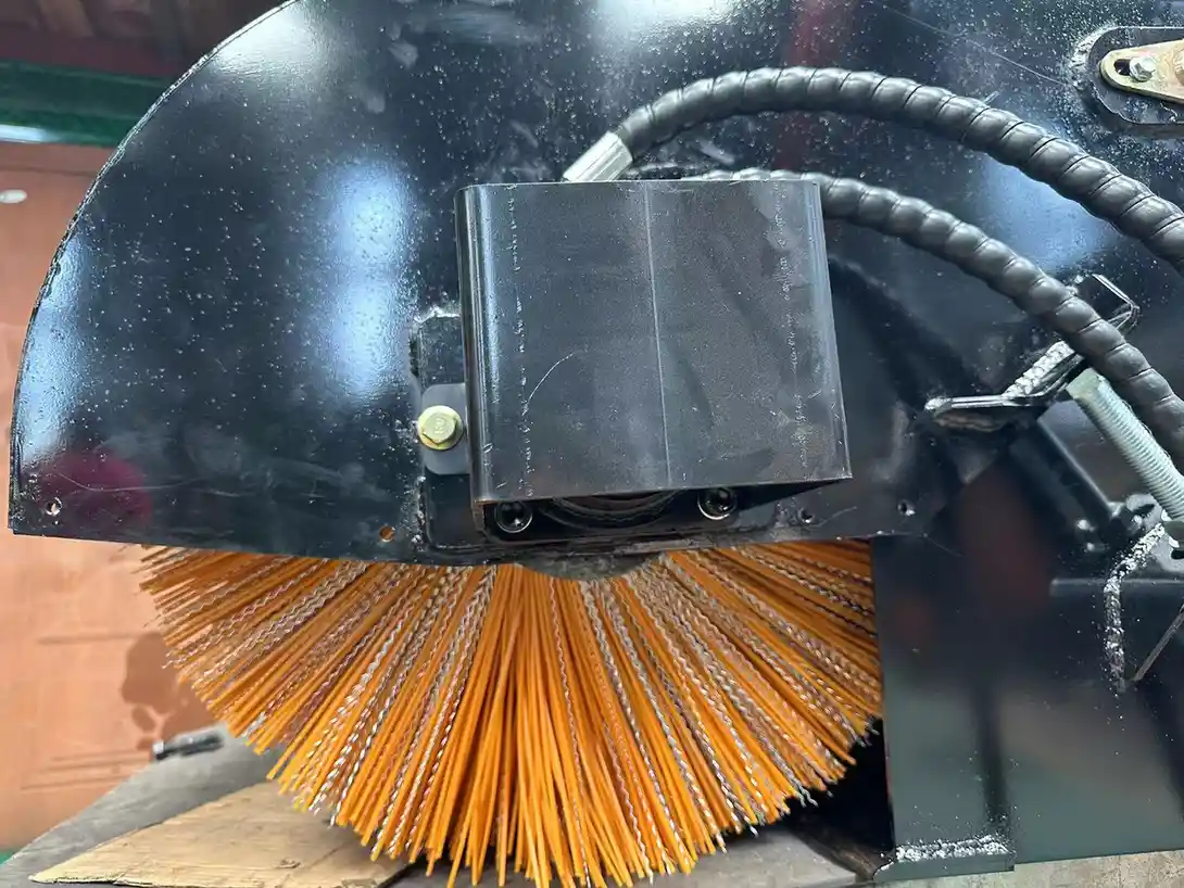 Rotary broom attachment showing bristles, drive housing and hydraulic hoses