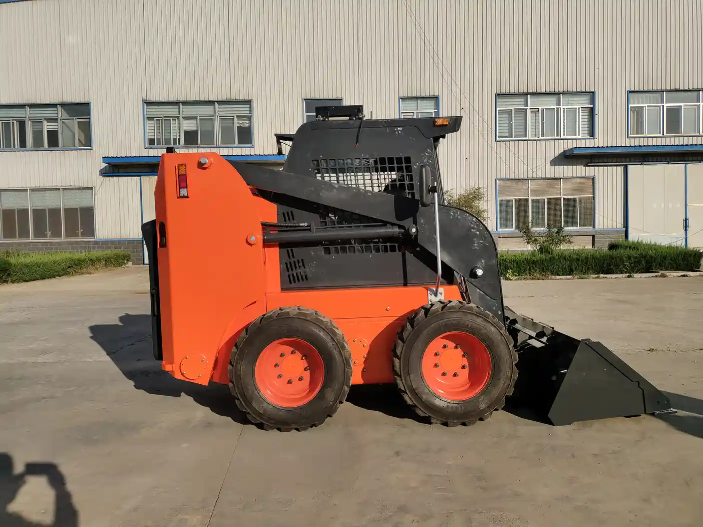 Side view of an orange wheeled skid steer loader with a front bucket